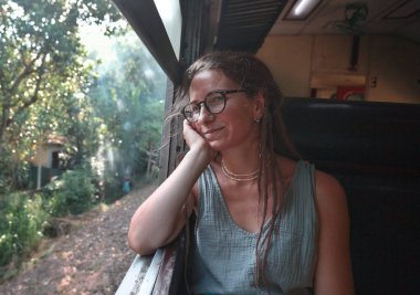 Sri Lanka 'nın dağlık bölgelerindeki çay tarlaları arasında Ella' dan Kandy 'ye tren yolculuğunun tadını çıkaran genç bir kadın.