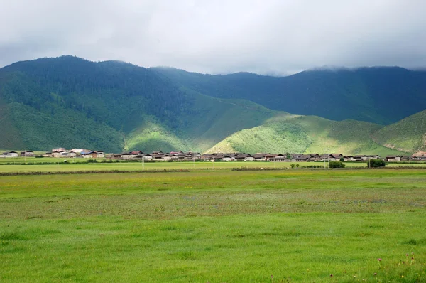 Yeşil dağlık mera ve mavi gökyüzünün altında Köyü. — Stok fotoğraf
