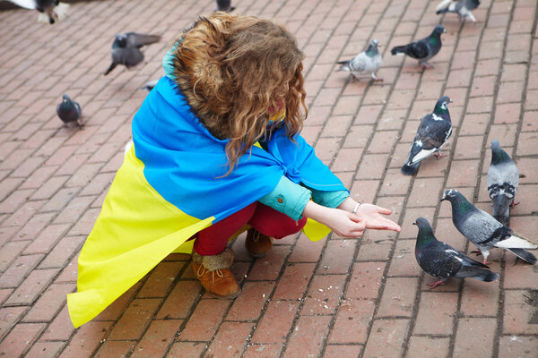 The girl with a flag feeds the pigeons on the square