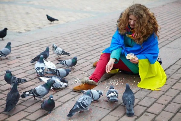 The girl with a flag feeds the pigeons on the square — Stock Photo, Image