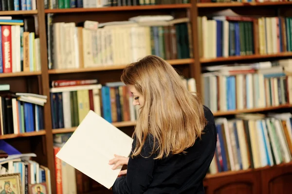 Uma jovem mulher na biblioteca lendo um livro — Fotografia de Stock