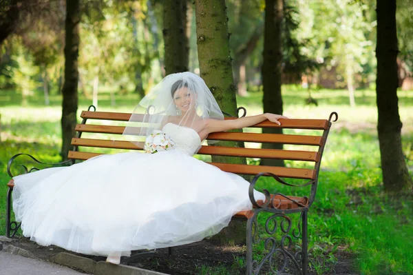 Attractive bride sitting on the bench in the park — Stock Photo, Image