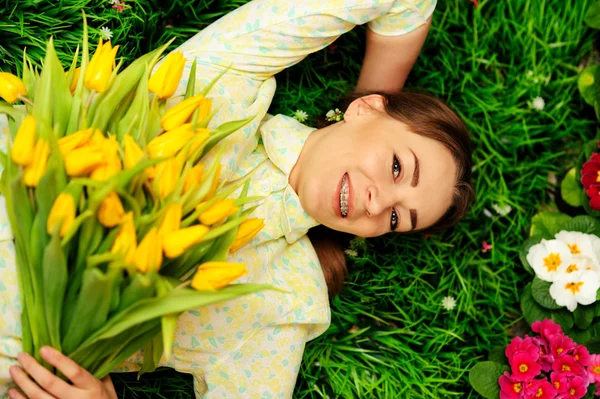 Menina bonito com flores na grama verde — Fotografia de Stock