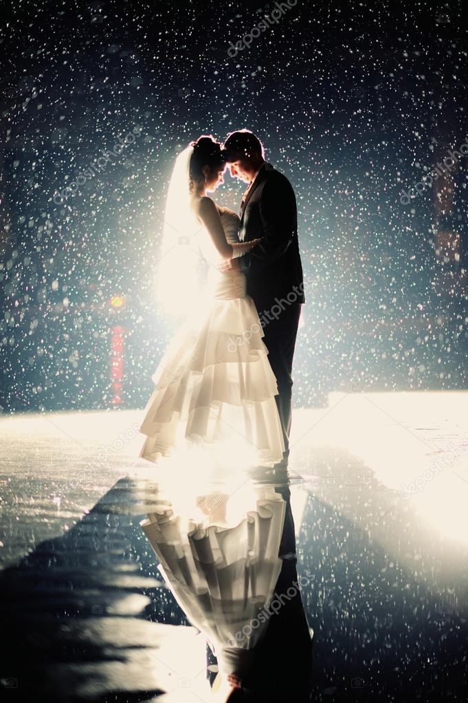 Bride and groom kissing under rain in the night
