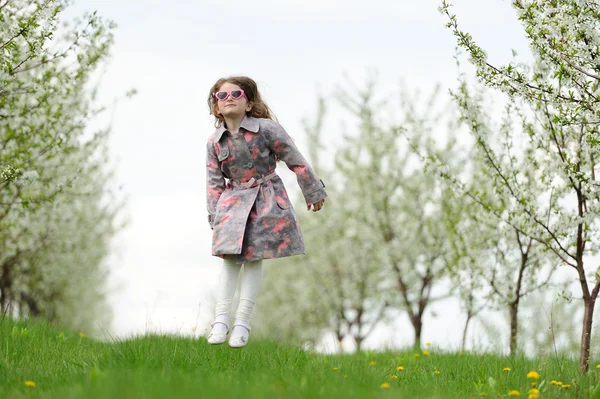 Pequena menina bonita pulando no jardim verde — Fotografia de Stock