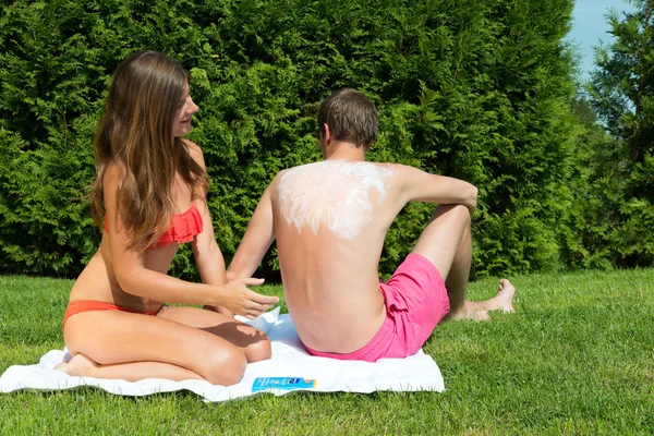 Mulher aplicando loção bronzeador no homem de volta — Fotografia de Stock