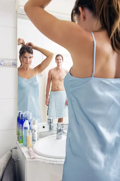 Spiegelbild eines jungen Mannes, der Frau beim Haaremachen im Badezimmer beobachtet — Stockfoto