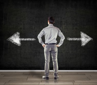 iki ok gösterilen beton duvarı önünde genç iş adamı