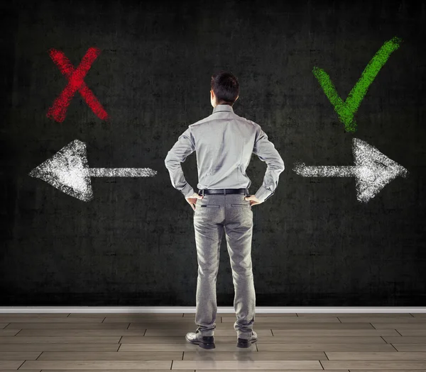 Young business man in front of a concrete wall showing two arrows — Stock Photo, Image