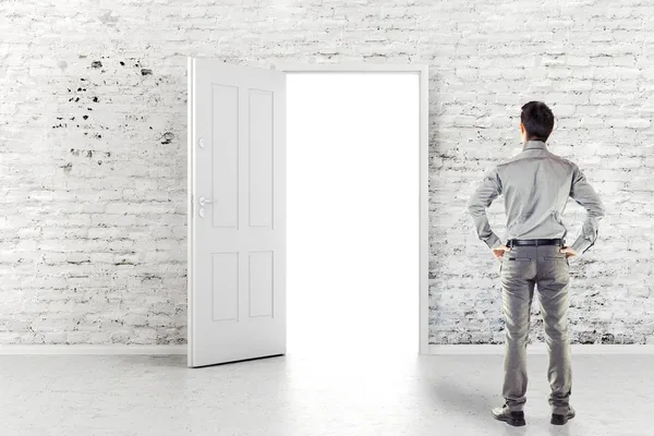 Joven hombre de negocios frente a una puerta abierta en una pared de ladrillo blanco vintage — Foto de Stock