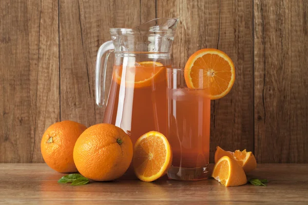 Suco de laranja fresco e laranjas no fundo de madeira vintage — Fotografia de Stock