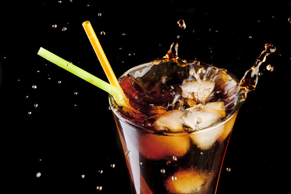 Fresh cola juice and ice cubes splash in a glass on black background