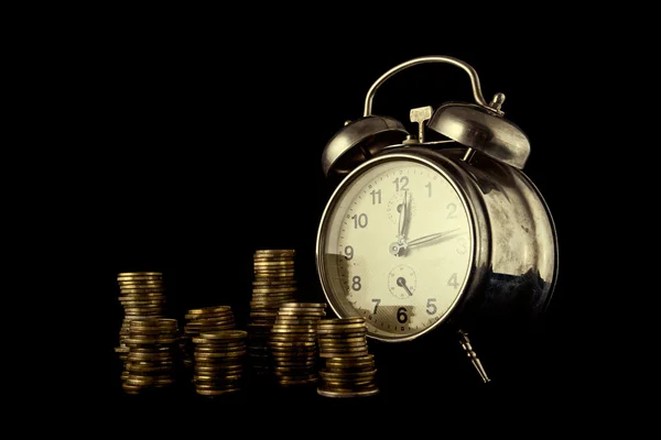 Gouden munt stack en vintage klok op donkere achtergrond Stockfoto