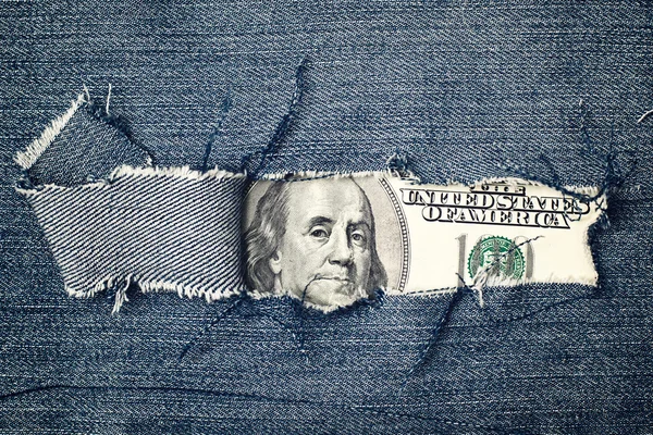 Hundred dollars bill through torn blue jeans texture — Stock Photo, Image