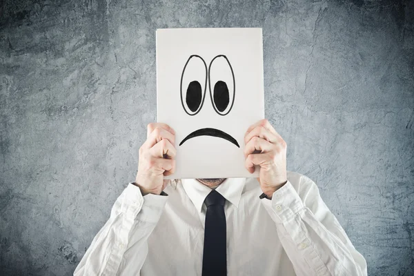 Businessman holding paper with sad face in front of his head — Stock Photo, Image