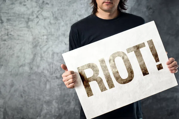 RIOT. Homem segurando cartaz com mensagem de protesto impresso — Fotografia de Stock