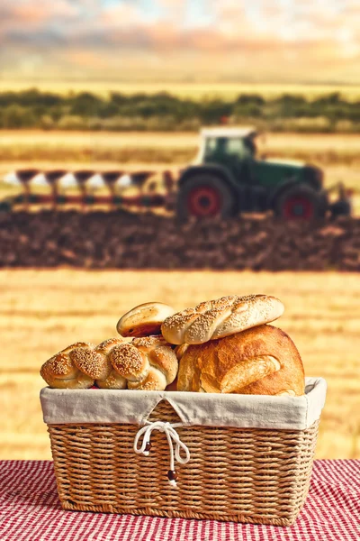 Bread in wicker basket with tractor and agricultural field in ba — Stock Photo, Image