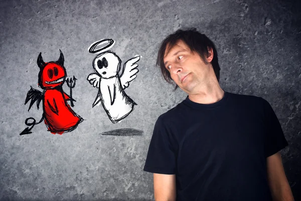 Casual man looking at doodle drawing of angel and devil fighting — Stock Photo, Image