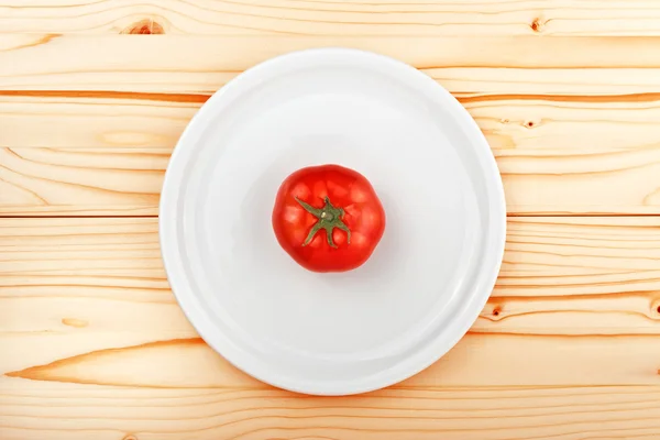 Verse rijpe tomaat geserveerd op wit bord op houten keukentafel — Stockfoto