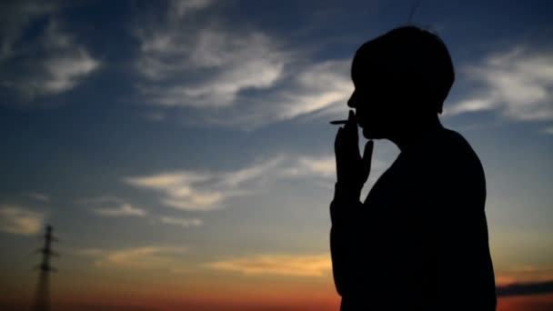 Силует молодої дорослої жінки, яка палить цигарку на заході сонця. 1920x1080 повний HD кадри . — стокове відео