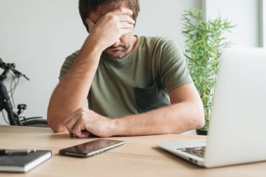 Ofis masasında hayal kırıklığına uğramış bir telekomünikasyon uzmanı yüzünü eliyle kapatıyor, seçici bir şekilde odaklanıyor.
