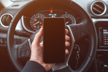 Araba sürücüsü cep telefonunu direksiyonun üzerinde tutuyor, kopyalama alanı olarak boş siyah ekran, seçici odak