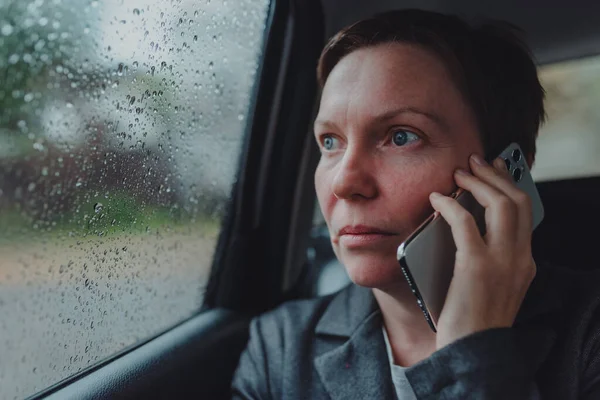 在雨中 一位严肃的女商人在车后座上用手机交谈 有选择地集中注意力 — 图库照片
