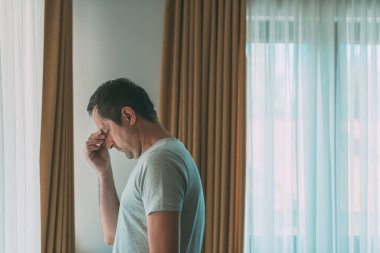 Depresyonda olan adam pencerenin yanında duruyor. Zihinsel sorunları olan üzgün erkek arkadaş, seçici odaklanma.