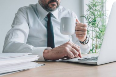 Ofiste kahve içmek, iş yerinde kahve fincanı ve laptopu olan bir iş adamı, seçici bir odak noktası.