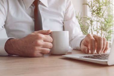 Ofis günü bir kahve, bir işadamı bardağı tutarak ve dizüstü bilgisayar kullanarak başlar.