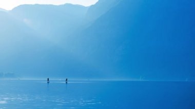 Cinemagraph footage of two people stand-up paddle boarding on lake, blue toned footage