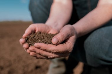 Hands of female farmer full of freshly ploughed fertile soil ground, close up with selective focus