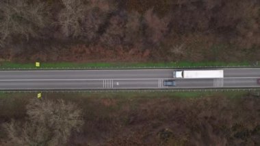 Aerial view of traffic on road through autumnal cottonwood forest, truck and cars on roadway from drone pov, directly above