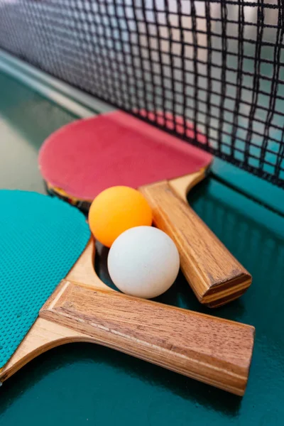 緑のテーブルの表面にテーブルテニスラケットとピンポンボールネット 選択的フォーカス — ストック写真
