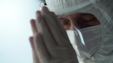 Medical professional in fully protective clothing praying, selective focus