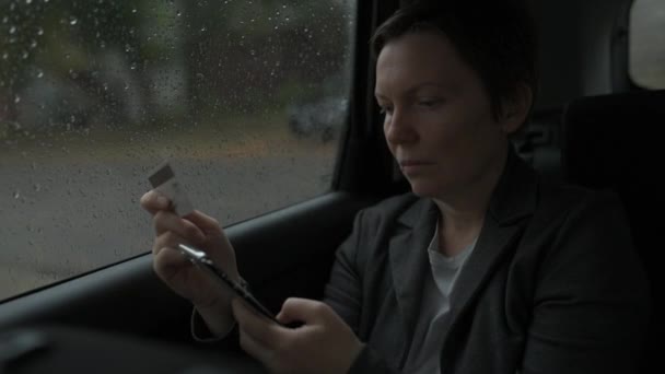 雨の中 車の後部座席から電子銀行のためのクレジットカードと携帯電話を使用してビジネスマンの女性 選択的な焦点 — ストック動画