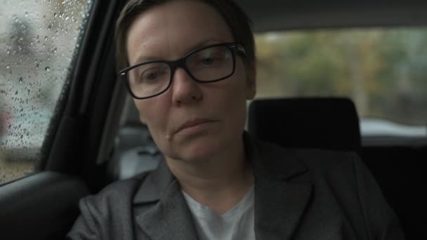 車の中で待っている眼鏡をかけ 雨の中窓の外を見て心配ビジネス女性 選択的な焦点 — ストック動画