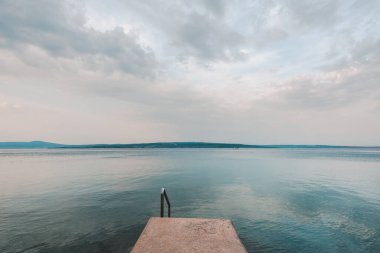Güneş doğarken deniz kıyısında beton iskele, arka planda Krk ve Adriyatik adası