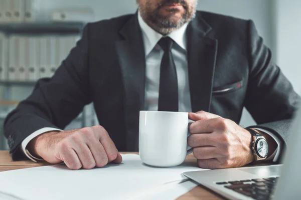 サラリーマンはオフィスの机で白いコーヒーカップを持っている 仕事中のカフェインの毎日の線量のためのコーヒーブレイク 選択的な焦点 — ストック写真