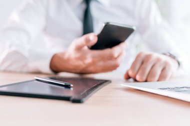 Stylus ve pad ofis masasında iş sözleşmelerinin e-imzalanması için, iş adamı arka planda akıllı telefon kullanıyor, seçici odaklanma