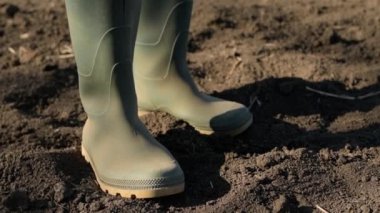 Kauçuk çizmeli kadın çiftçinin tarlada dikilirken, seçici bir odak noktası var.