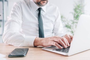 Ofiste dizüstü bilgisayar kullanan erkek girişimci, portatif bilgisayar klavyesini seçici bir odak ile yazarken elleri yakın plan