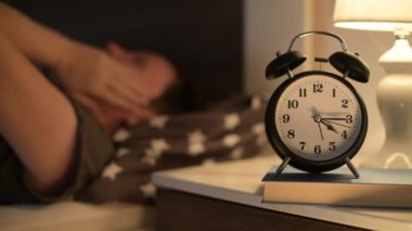 Uykusuz uykusuz kadın yatakta uzanıyor ve komodinin üzerindeki çalar saate bakıyor, seçici odaklı.