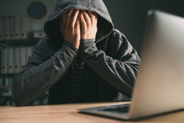 Üzüntülü bilgisayar korsanı elleri dizüstü bilgisayarın önünde olan yüzünü kapatıyor, seçici odaklanma
