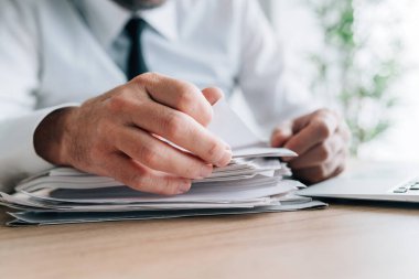 Çalışan adaylarını okuyan İK yöneticisi ofis masasına yığılmış, seçici odaklı özgeçmişine devam ediyor