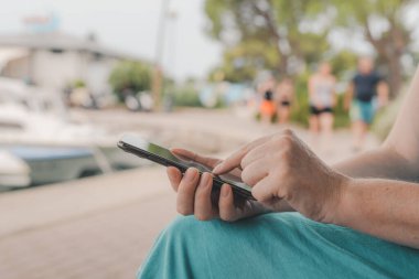 Parkta akıllı telefon kullanan bir kadın, cep telefonuyla kadın ellerini kapatıyor, seçici bir şekilde odaklanıyor.