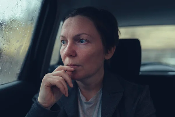 仕事に向かう途中の寒い雨の日にタクシーの窓から外を見る失望と心配のビジネスマン女性 選択的フォーカス — ストック写真
