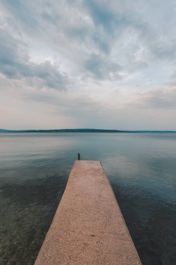 Güneş doğarken deniz kıyısında beton iskele, arka planda Krk ve Adriyatik adası