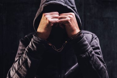 Kelepçeli, yüzünü saklayan, seçici odaklı bir suçlu.