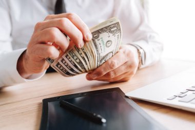 İş adamı önemsiz nakit sayıyor. Ofiste Amerikan doları banknotları, seçici odaklanma.